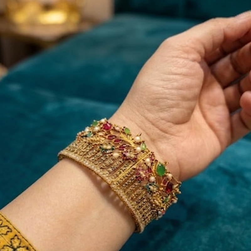 Gold bracelet with colorful stones on a hand against a teal fabric background