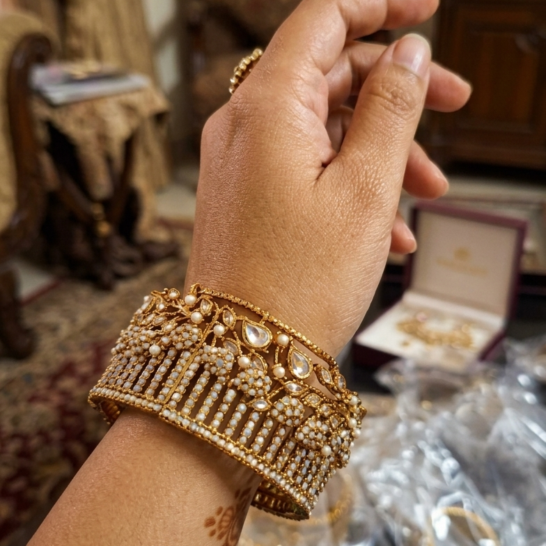 Hand wearing a gold bracelet with jewelry box and items in the background